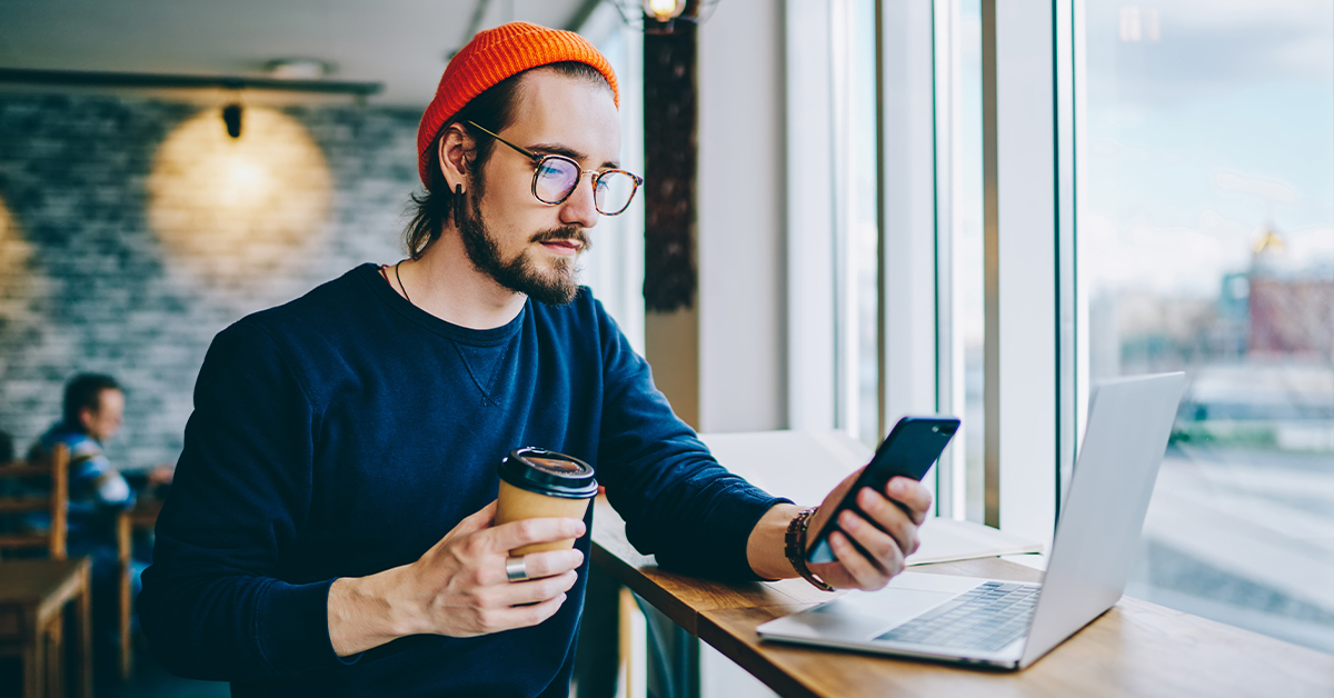 Man with smartphone and laptop in coffee shop