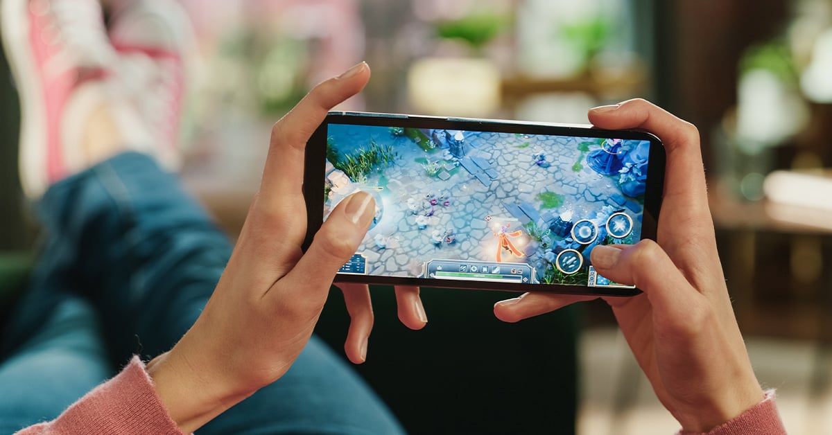 Close-up of person playing a multiplayer mobile game on a smartphone while relaxing indoors